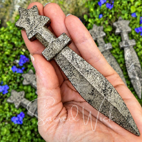 Pyrite crystal athame held in hand to show its 5.25 inch size, metallic finish, star-shaped handle, crossguard, and pointed carved blade.