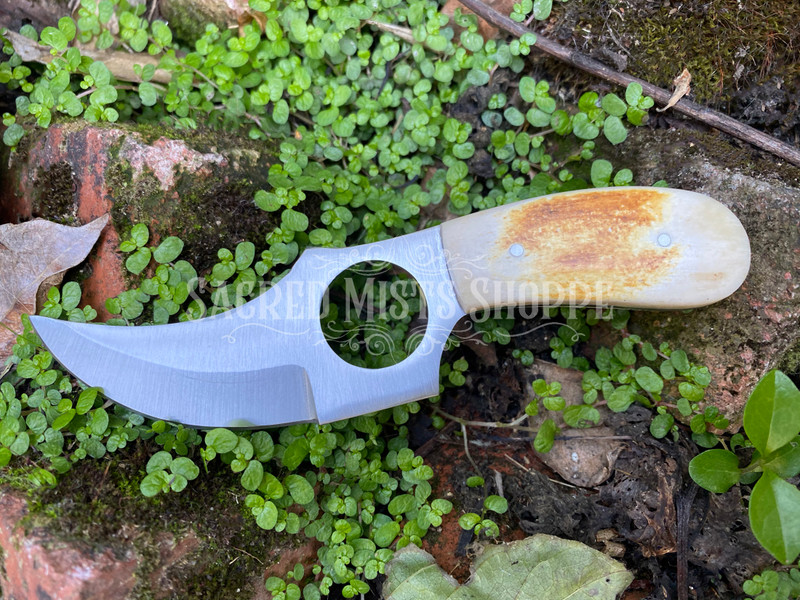 The Sacred Circle Boline is crafted with a beautiful bone handle and features a beautiful curved and sharpened blade with a circle cut out. This knife is perfect for cutting herbs and other items used in herbalism recipes or for the witch's altar use. This beautiful and unique boline comes complete with a decorative sheath for blade protection and safe storage.