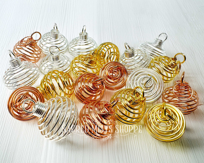 an assortment of wire coil cages for jewelry making in gold, silver, and copper colors on a light colored table.