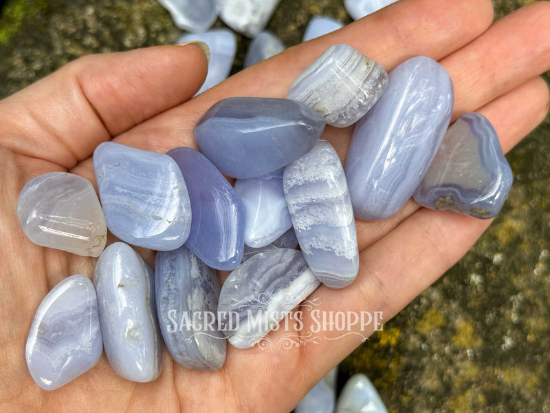 Several blue lace agate tumbled crystals resting across an open palm with greenery in the background, showing size and natural beauty.