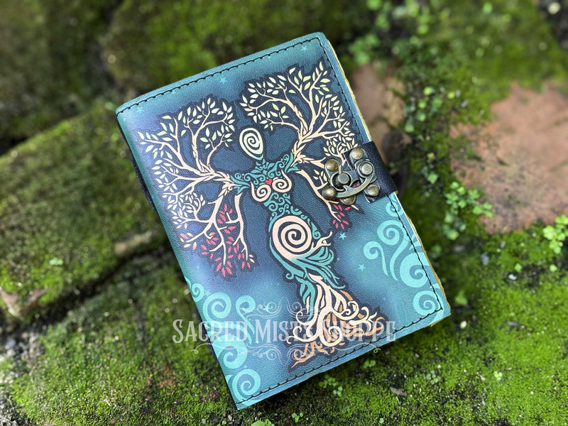Overhead view of one green leather Tree of Life Goddess journal lying closed on moss-covered brick, highlighting the natural tones and artistry.