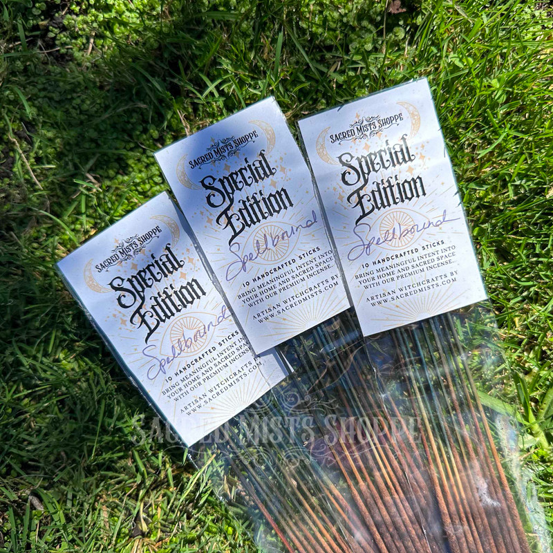 Three packages of Sacred Mists Shoppe Spellbound artisan incense sticks arranged diagonally on green grass in natural sunlight.