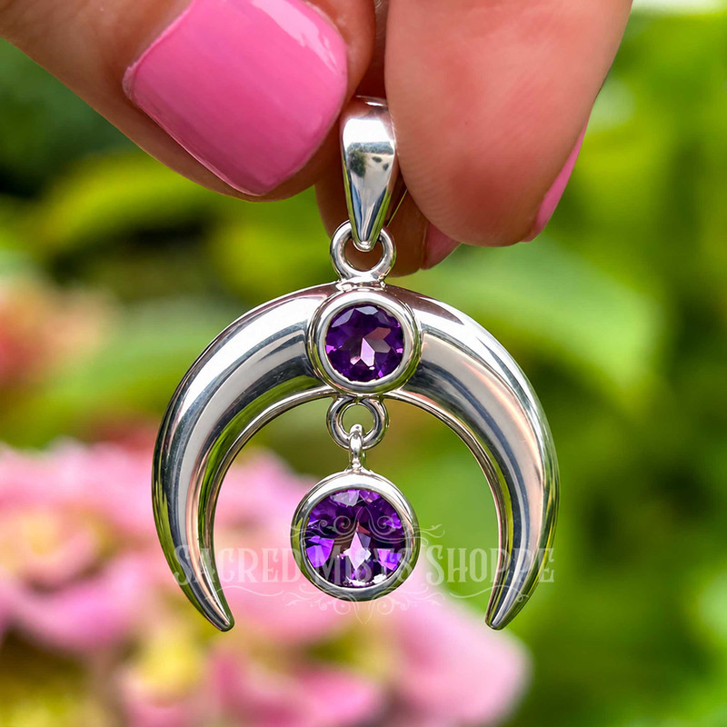 Amethyst crescent moon pendant held upright, showing the polished sterling silver crescent and freely hanging faceted Amethyst.