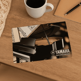 A cleaning microfibre cloth featuring a piano, placed on a wooden table with a coffee cup and pen. A cleaning microfibre cloth featuring a piano, placed on a wooden table with a coffee cup and pen.