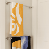 A yellow bath towel with a pattern hangs above a black towel featuring a design, both on a towel rack. A yellow bath towel with a pattern hangs above a black towel featuring a design, both on a towel rack.