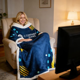 A woman sits in a chair, wrapped in a navy blue blanket with yellow and green patterns, enjoying a show on TV.