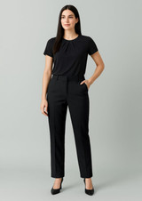 A woman wearing black tapered adjustable waist pants and a black top, standing with hands in pockets against a neutral background.