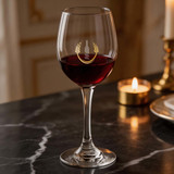 A wine glass with a stem, featuring a logo, filled with red wine, set on a dark marble surface.