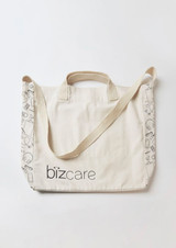 A cream tote bag with a strap, featuring a logo and patterned detailing along the edges.
