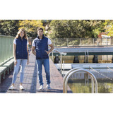 A navy blue unisex puffer vest displayed on two models by a waterfront. The vest features a logo.