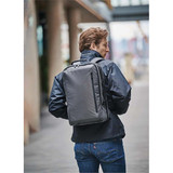 A person wearing a black jacket carries a grey Hedmark Commuter Backpack on their back in an outdoor setting.