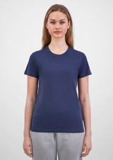 A woman stands wearing a navy short sleeve tee, paired with grey sweatpants, featuring a logo on the tee.