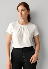 A woman wears a white short sleeve top with a pleat design, paired with black trousers and holding a clutch.