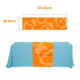 A medium table runner in vibrant orange with a circular design, featuring a logo, set against a blue tablecloth.