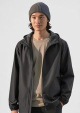 A grey rain jacket is worn by a person with dark hair, complemented by a grey beanie and a beige shirt underneath.