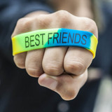 A vibrant silicone wristband in yellow, green, and blue, featuring "BEST FRIENDS" text. The design includes a logo.