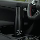 A drink bottle in matte black with a logo, placed in a car cup holder. A drink bottle in matte black with a logo, placed in a car cup holder.