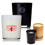 A black and white candle in various holders, featuring a logo, with one candle in a cardboard cylinder.