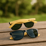 Sunglasses featuring a black frame with green lenses and yellow bamboo arms, displayed on a wooden surface.