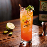 A glass tumbler filled with a colourful cocktail, garnished with mint and a lemon slice, on a wooden surface.