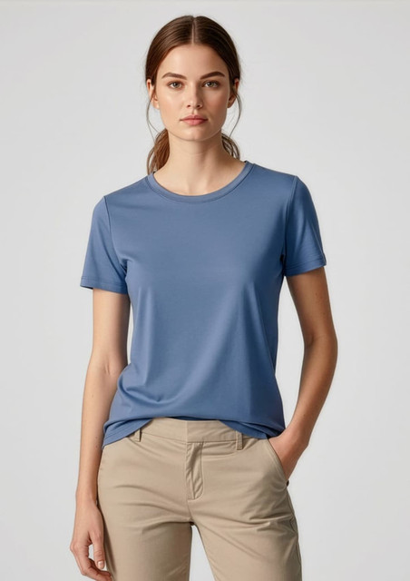 A women's short sleeve tee in blue, made from a smooth fabric, paired with light-coloured pants. The shirt features a logo.