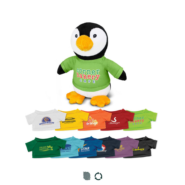 A penguin plush toy with an orange beak and feet, wearing a green shirt, surrounded by various colourful t-shirts.