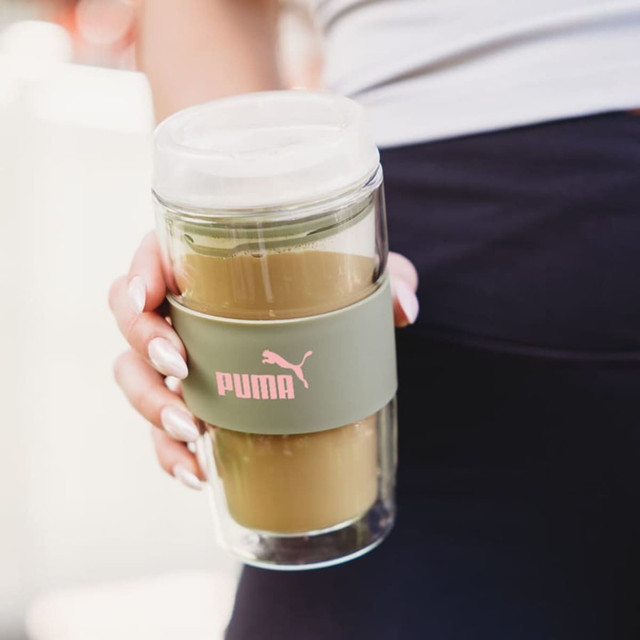 A reusable coffee cup featuring a clear body, green silicone band, and a lid, with a logo.