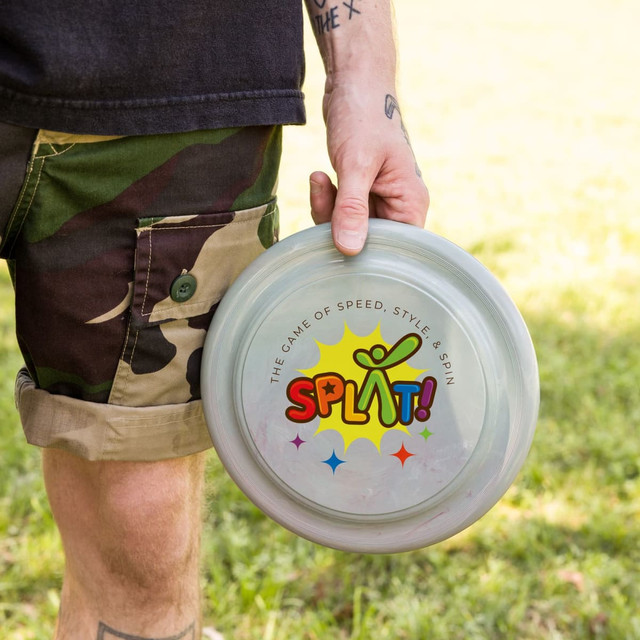 A grey frisbee is held in hand, featuring a colourful logo with playful text and a design.