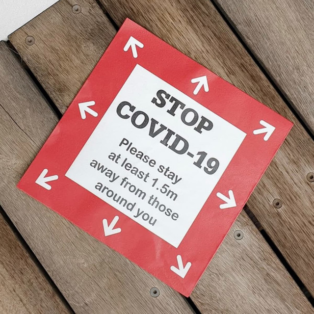A floor decal sticker with a red background and white arrows, featuring text about staying 1.5m apart.