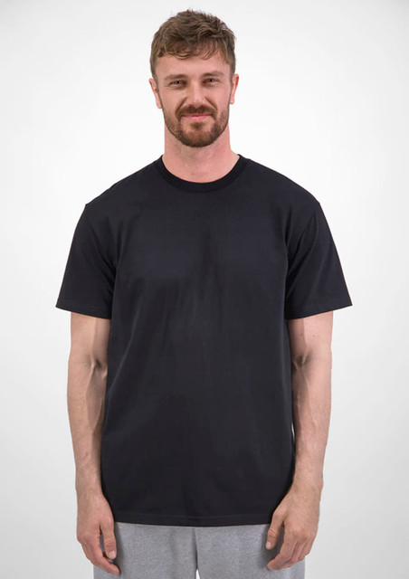 A man stands wearing a plain black short sleeve tee, with a neutral background. The tee features a logo.