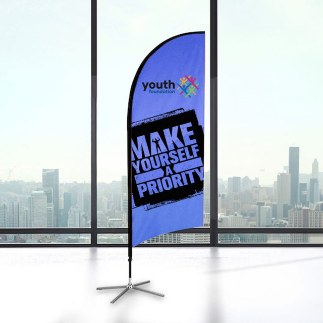 A small feather flag kit featuring a blue background and a logo, displayed indoors with a city skyline view.