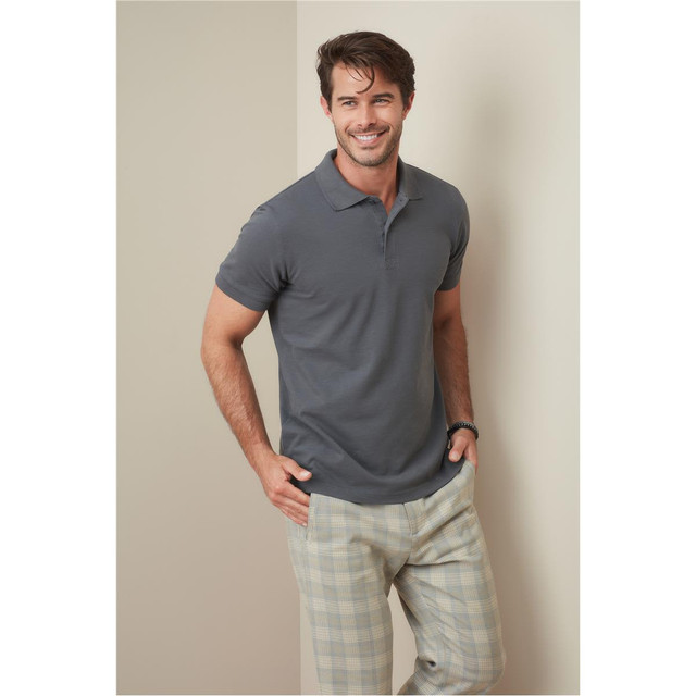 A man wearing a grey polo shirt stands confidently, paired with light-coloured checkered pants, in a neutral setting.