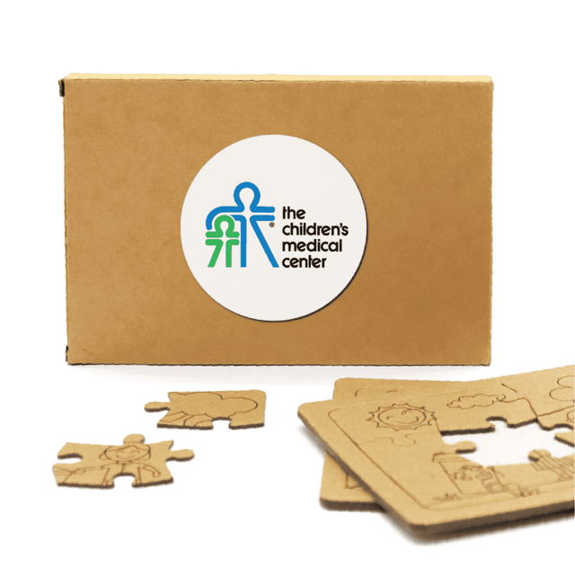A cardboard box containing wooden jigsaw puzzle pieces, featuring a logo and light brown tones.