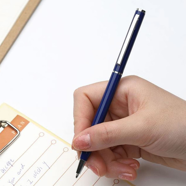 A hand holding a silver and blue metal pen, poised over a notepad with handwritten notes.