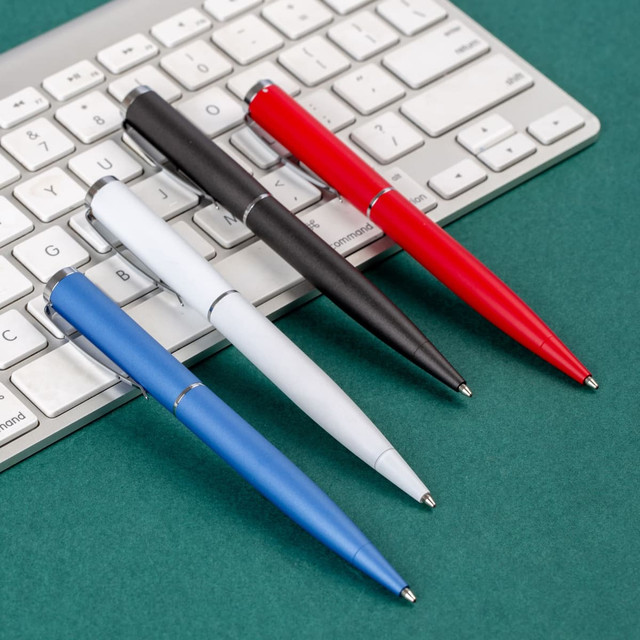 Metal pens in blue, white, black, and red placed on a grey keyboard against a green background.