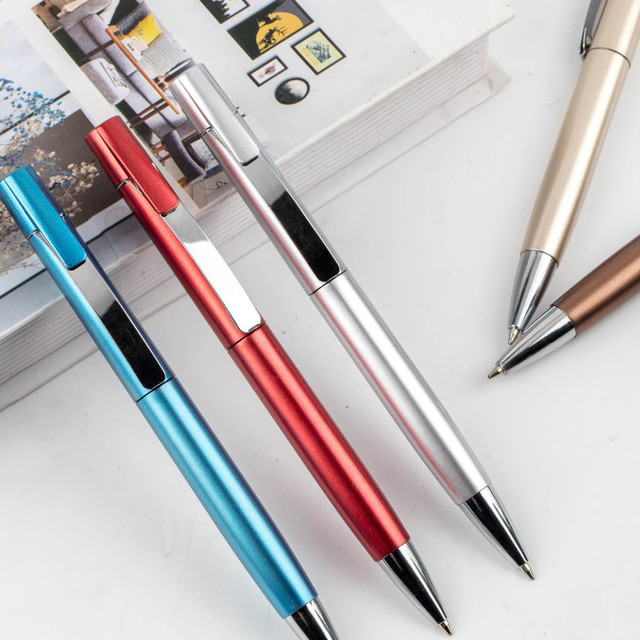 A set of metal pens in blue, red, silver, and bronze, resting beside a stack of books. Each pen has a branding logo.