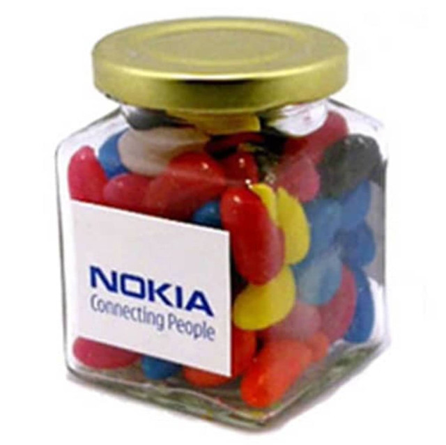 A glass square jar filled with colourful mini jelly beans, featuring a gold lid and a logo on the jar.