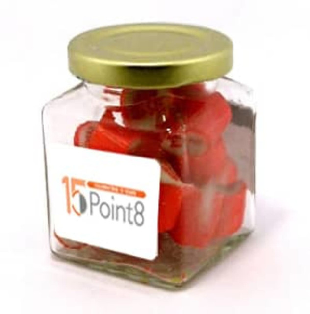 A square glass jar filled with red rock candy, topped with a gold lid and featuring a logo.