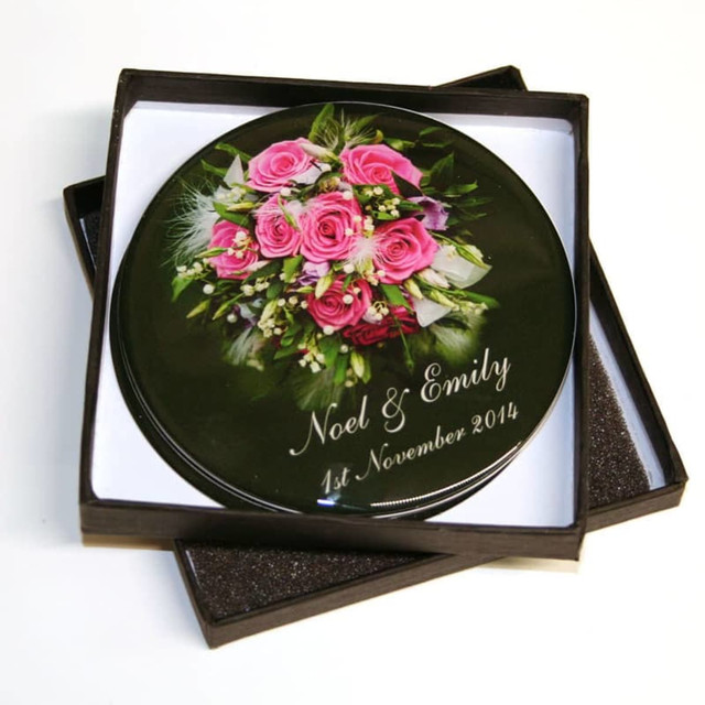 A round, black coaster featuring a floral design with pink roses, presented in a square box.