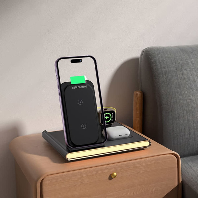 A magnetic wireless charger in black, positioned next to a phone on a wooden bedside table, with a small notebook and earbuds.