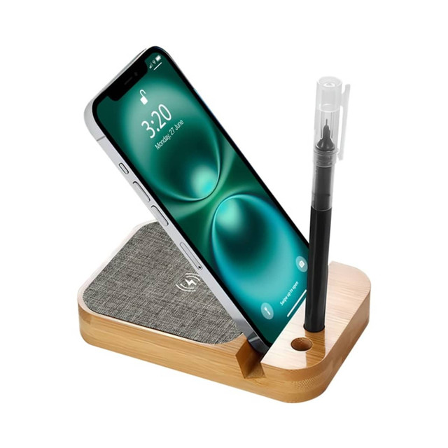 A wooden wireless charger with a grey fabric pad, holding a smartphone and a pen. It features a logo on the base.