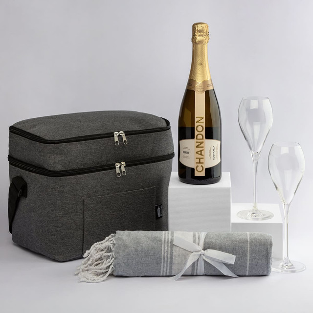 A grey cooler bag, champagne bottle, two glass flutes, and a grey blanket with white stripes. The bag features a logo.