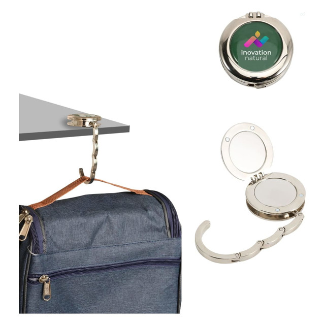 A foldable desk hook with a mirror, featuring silver metal and a logo, displayed with a backpack and attached to a table.