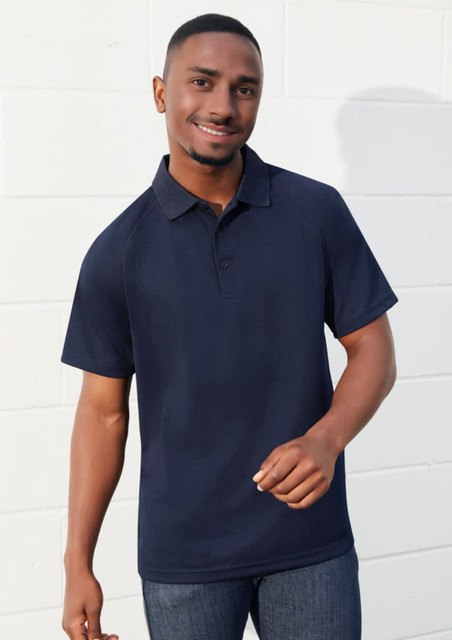 A navy short sleeve polo shirt with a collar and a logo, worn by a smiling man against a white wall. A navy short sleeve polo shirt with a collar and a logo, worn by a smiling man against a white wall.