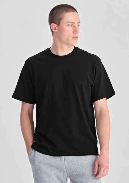 A black box tee worn by a model standing with hands in pockets, featuring a simple design and a relaxed fit.