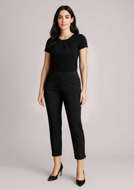 A woman stands in slim black mid-waist pants paired with a black top and heels, featuring a logo on the pants.