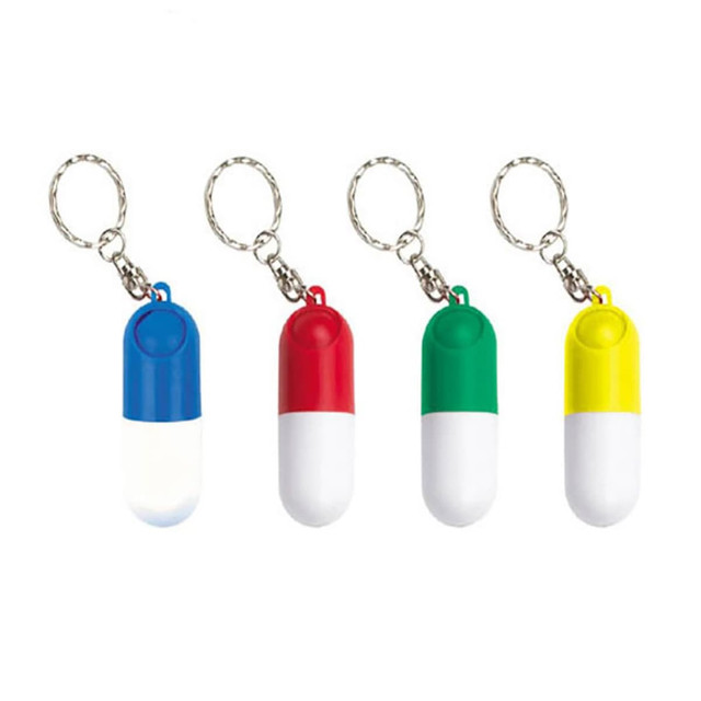 A set of four capsule-shaped pill boxes in blue, red, green, and yellow, each with a keyring attachment. A set of four capsule-shaped pill boxes in blue, red, green, and yellow, each with a keyring attachment.