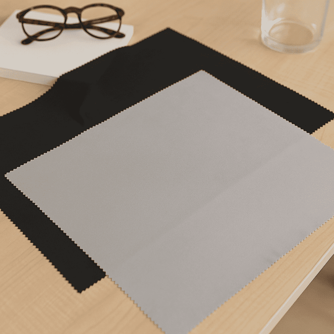 A large microfibre cloth in grey and black, placed on a wooden table with glasses and a glass of water.
