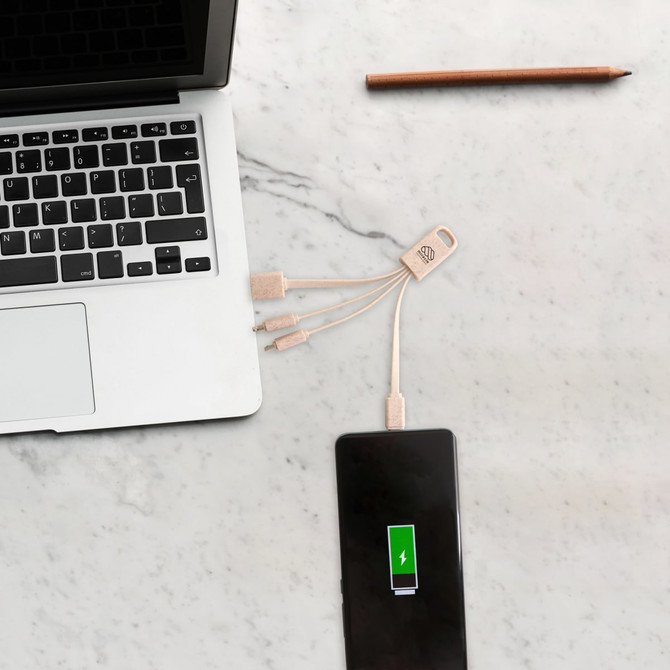 A square-shaped wheat straw charging cable in beige connects a phone to a laptop on a marble surface.
