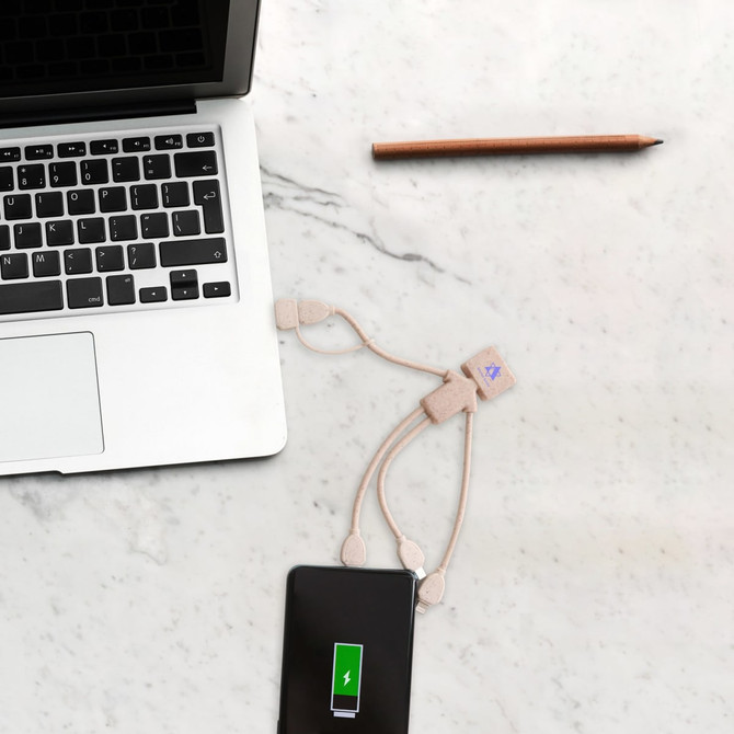 A wheat straw charging cable in a man shape, in beige, connected to a smartphone and a laptop on a marble surface.